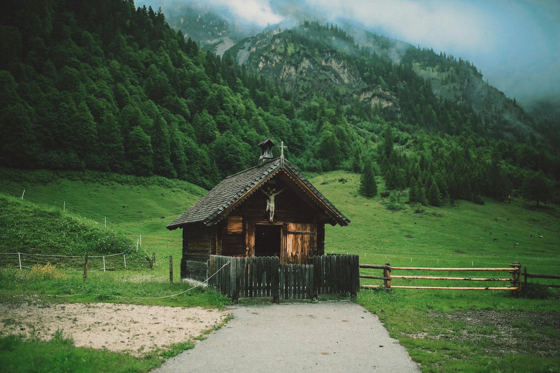 A picture of a small wooden cabin with lush green hills behind it. 