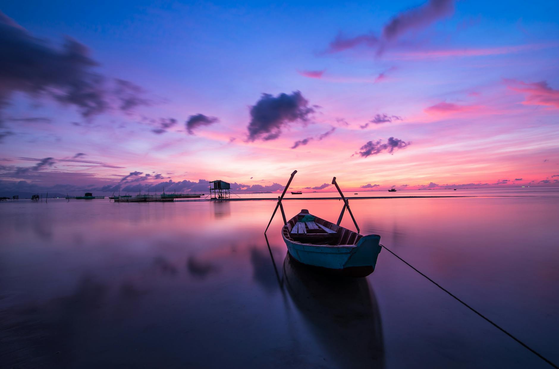 A picture of an empty boat on the ocean, with a purple pink sky due to the sun setting. 