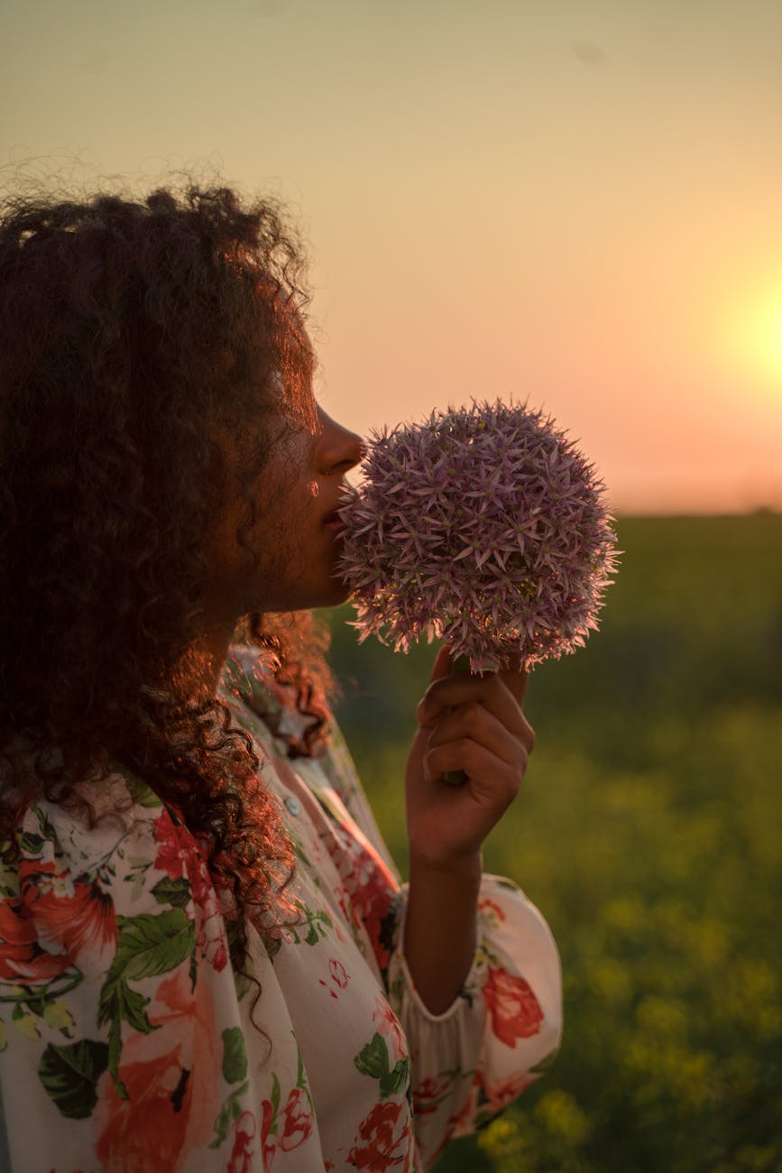 Fem-presenting person of color smelling flowers as the sunt sets